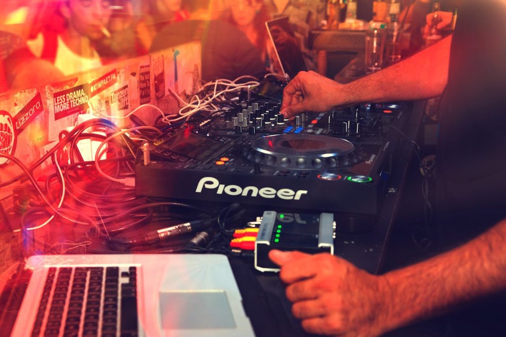 DJ operating a mixer during a lively nightclub party with vibrant lights.