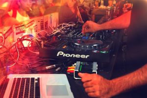 DJ operating a mixer during a lively nightclub party with vibrant lights.